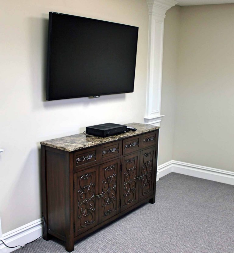 A wall-mounted television above a carved wooden console