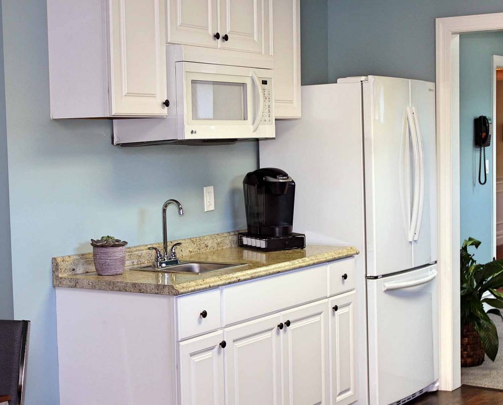 A kitchen with white cabinets, a sink, a microwave, a coffee maker and a refrigerator