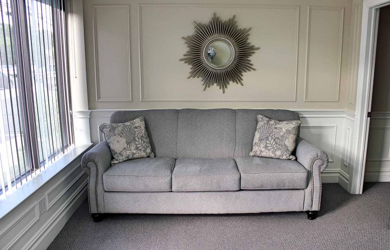 A grey sofa with patterned cushions beneath a sunburst mirror